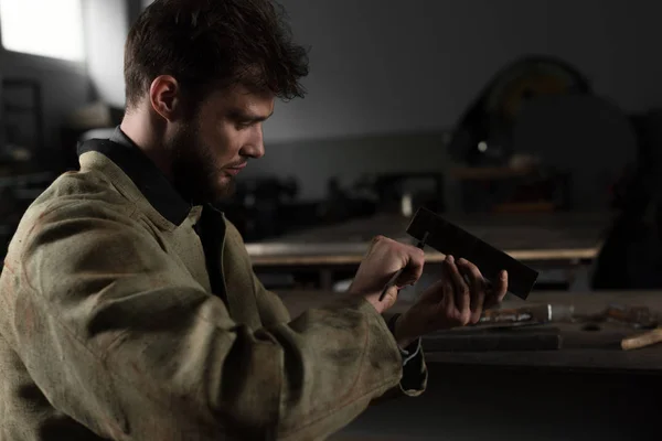 Side view of young male worker measuring metal part at factory — Stock Photo