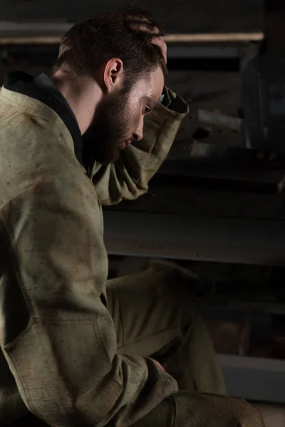 Vue latérale du jeune travailleur masculin fatigué assis à l'usine — Photo de stock