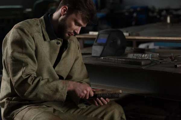 Ouvrier masculin en uniforme nettoyage partie métallique par brosse à l'usine — Photo de stock