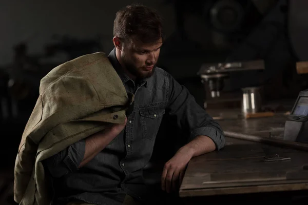 Junger Arbeiter sitzt am Tisch mit Uniform auf der Schulter — Stockfoto