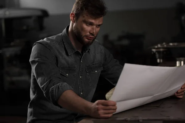 Young male worker sitting and looking at blueprint — Stock Photo