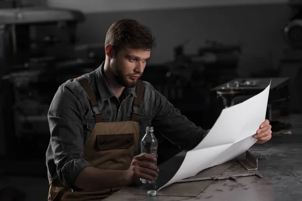 Trabalhador sentado com garrafa de água e olhando para o modelo — Fotografia de Stock
