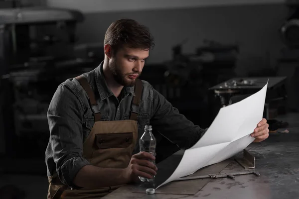 Operaio seduto con bottiglia d'acqua e guardando cianografia — Foto stock