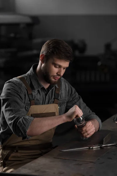 Young male worker sitting at table and opening bottle of water at factory — Stock Photo