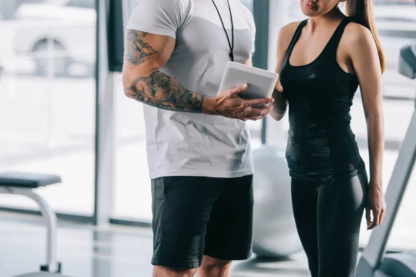 Imagen recortada de entrenador personal masculino mostrando horario en la tableta digital a la deportista en el gimnasio - foto de stock