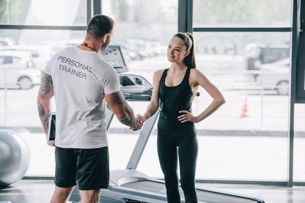 Vista trasera de entrenador personal masculino y joven deportista estrechando la mano en el gimnasio - foto de stock