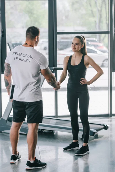 Rear view of male personal trainer and young sportswoman shaking hands at gym — Stock Photo