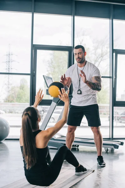 Male personal trainer and sportswoman doing exercises with ball at gym — Stock Photo