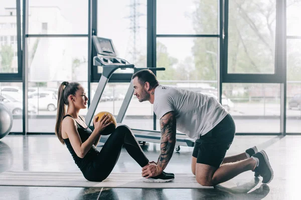 Männlicher Personal Trainer hilft Sportlerin beim Bauchmuskeltraining mit Ball im Fitnessstudio — Stockfoto