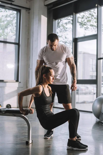 Entraîneur personnel masculin regardant sportive faisant planche à la salle de gym — Photo de stock