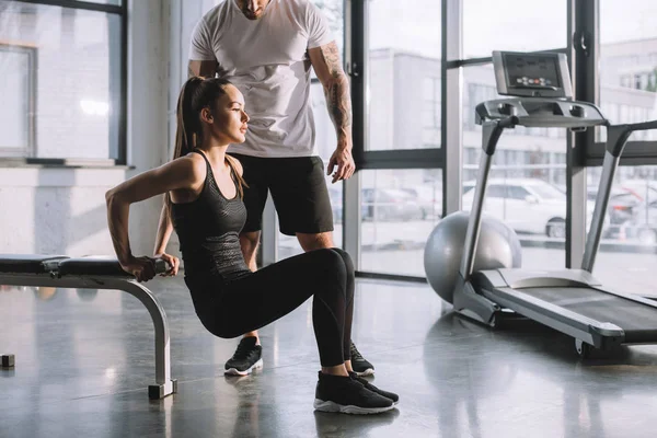 Male personal trainer looking at sportswoman doing plank at gym — Stock Photo