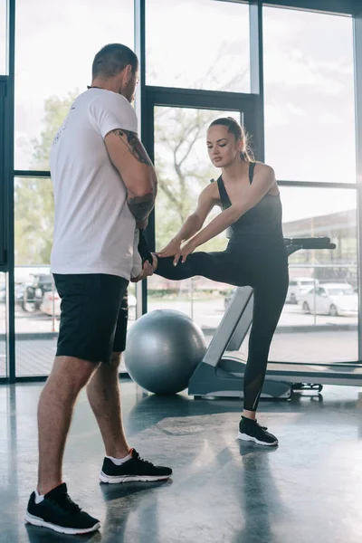 Male personal trainer helping sportswoman to stretching at gym — Stock Photo