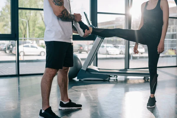 Entrenador personal masculino ayudando a la deportista a estirarse en el gimnasio - foto de stock