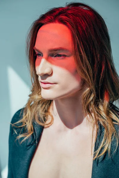 Handsome man with long hair and red light on face, on grey — Stock Photo