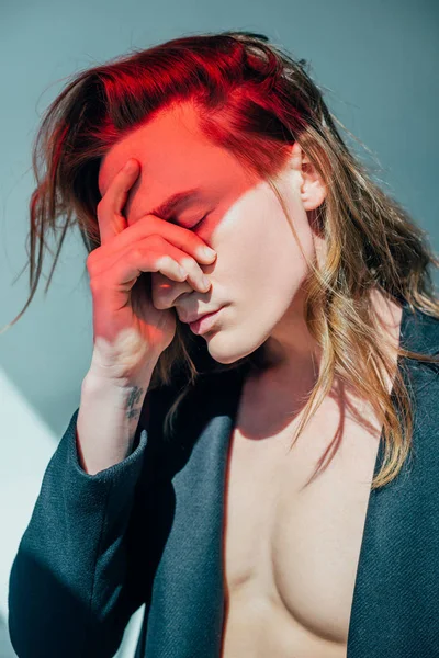 Hombre cansado con el pelo largo y luz roja en la cara, en gris - foto de stock