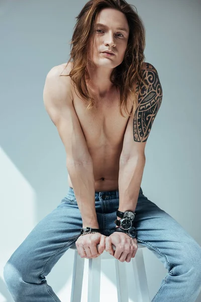 Сексуальный мужчина без рубашки с длинными волосами и татуировкой на руке, на сером — стоковое фото
