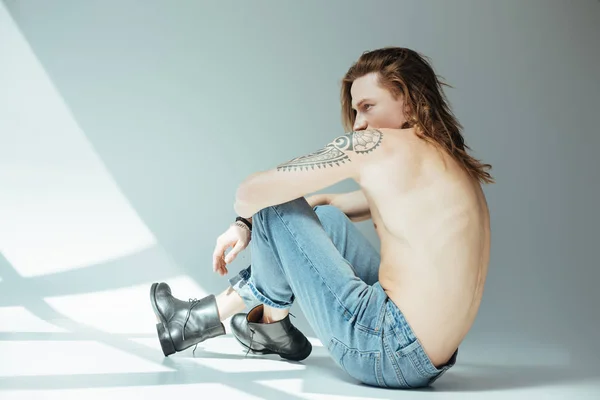 Sexy Mann ohne Hemd mit langen Haaren posiert in Jeans, auf grau — Stockfoto