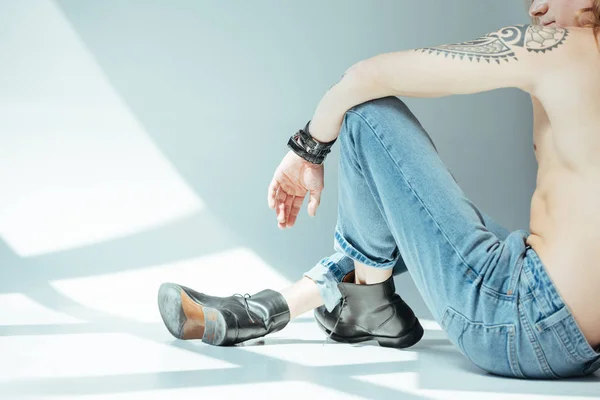 Обрезанный вид сексуального мужчины, сидящего в джинсах, на сером — стоковое фото