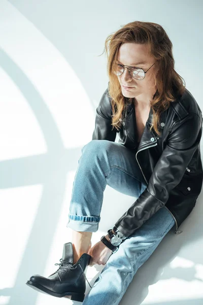 Elegant man posing in eyeglasses, jeans and black leather jacket, on grey — Stock Photo