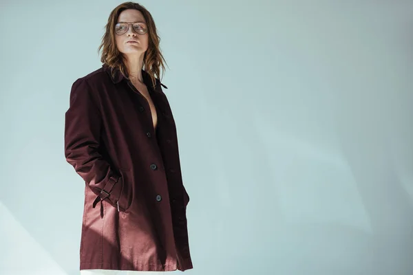 Stylish elegant man in glasses posing in trench coat, isolated on grey — Stock Photo