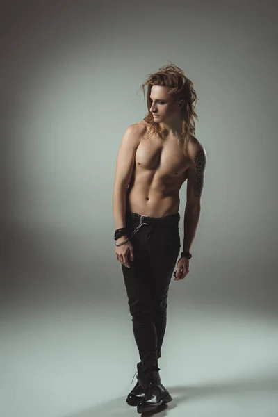 Shirtless man with long hair posing in black jeans, on grey — Stock Photo