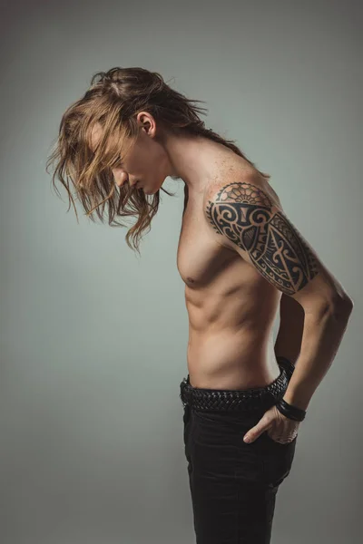 Sexy hombre sin camisa con tatuaje posando en pantalones vaqueros negros, aislado en gris - foto de stock