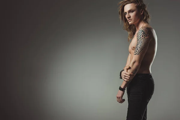Handsome shirtless man with tattoo posing in black jeans, isolated on grey with copy space — Stock Photo