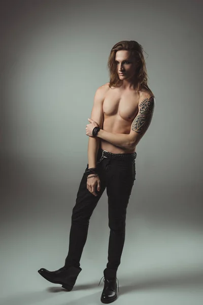 Schöner hemdloser Mann mit Tätowierung posiert in schwarzen Jeans, auf grau — Stockfoto