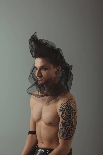 Татуйований чоловік з дивною зачіскою і чорною сіткою на голові, ізольований на сірому — стокове фото