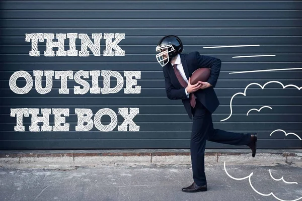 Side view of businessman in suit and rugby helmet with ball in hands running on street with think outside box inscription — Stock Photo