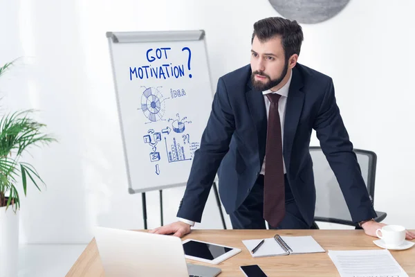Cher homme d'affaires regardant loin sur le lieu de travail au bureau avec une inscription de motivation et des graphiques d'affaires sur tableau blanc — Photo de stock