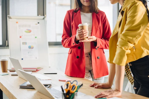 Geschäftsfrau hält Kaffeetasse in der Hand und hört ihrem Kollegen am Arbeitsplatz zu — Stockfoto