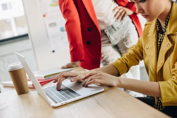 Asian woman typing on laptop keyboard by her colleague in modern office — Stock Photo