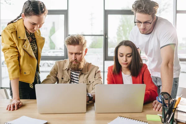 Diverse business team working on project and looking on laptop screens in light workspace — Stock Photo