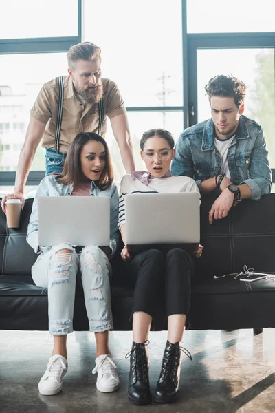 Equipo de negocios diverso que mira las pantallas de los ordenadores portátiles en el espacio de trabajo ligero - foto de stock