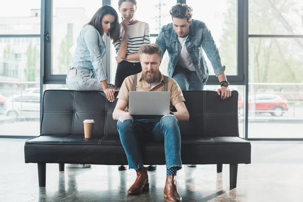 Profissionais de negócios olhando para seu colega masculino trabalhando no laptop no escritório moderno — Fotografia de Stock