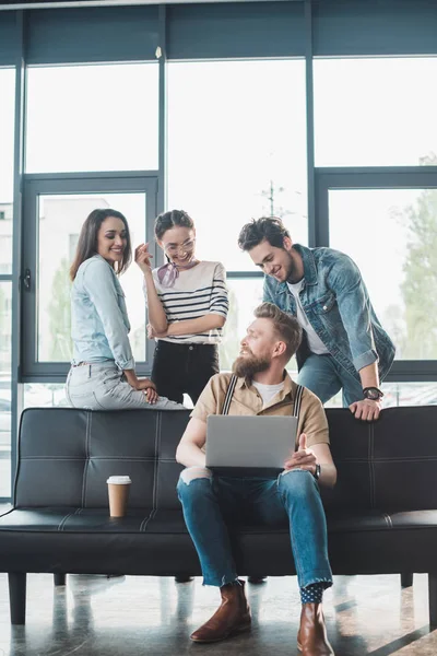 Uomo d'affari e donne che guardano il loro collega di sesso maschile che lavora su laptop in un ufficio moderno — Foto stock