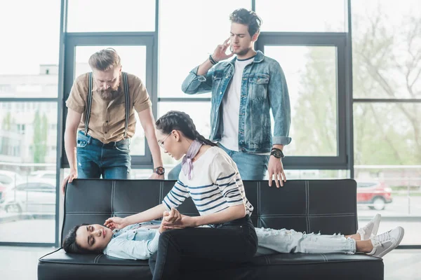 Business colleagues helping young fainted woman lying on sofa in office — Stock Photo