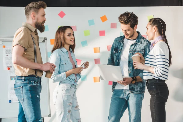 Diverse business team with laptop by white board with sticky notes in light workspace — Stock Photo