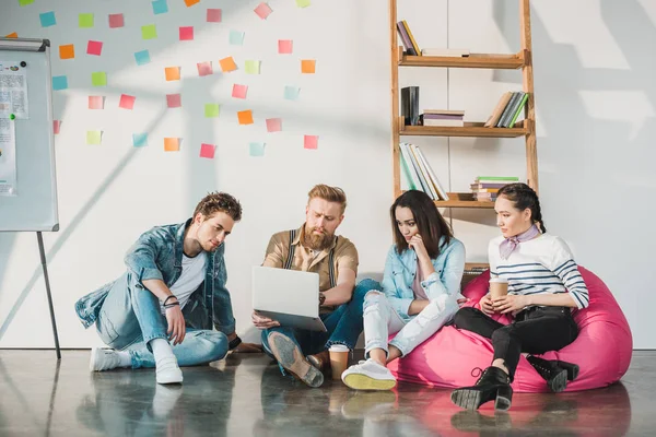 Professional business colleagues men and women sitting on floor and looking at laptop in modern office — Stock Photo