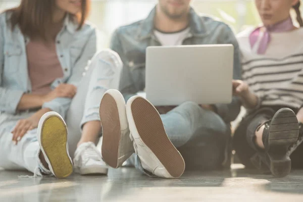 Cropped view of coworkers sitting on floor with laptop in light workspace — Stock Photo