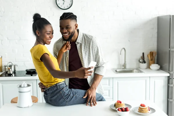 African american couple taking selfie with smartphone at kitchen — Stock Photo