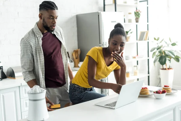 Chocado casal afro-americano olhando para laptop na cozinha — Fotografia de Stock