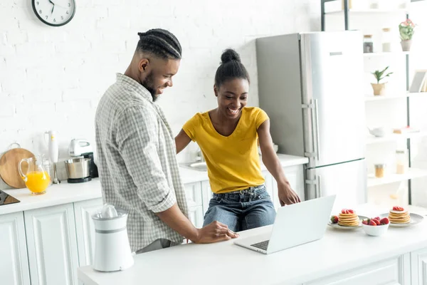 Sonriente africano americano pareja mirando portátil en cocina - foto de stock