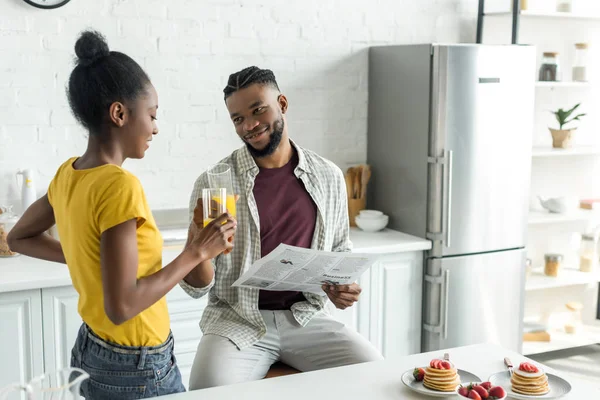 Pareja afroamericana tintineo con vasos de jugo de naranja en la cocina — Stock Photo