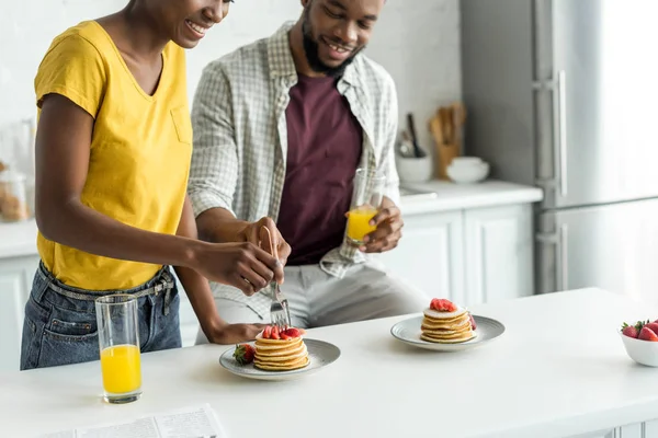 Abgeschnittenes Bild eines afrikanisch-amerikanischen Paares, das Pfannkuchen isst und Orangensaft in der Küche trinkt — Stockfoto
