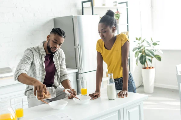 African american boyfriend pouring out cornflakes into plate at kitchen — Stock Photo