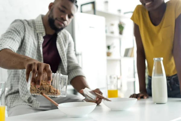 Immagine ritagliata del fidanzato afroamericano versando cornflakes nel piatto in cucina — Foto stock