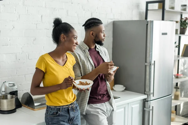 Sorrindo casal afro-americano tomando café da manhã na cozinha e olhando para longe — Fotografia de Stock