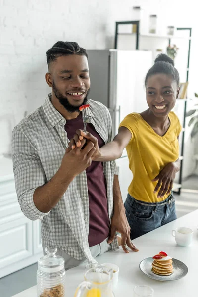 Sorrindo casal afro-americano com morango em garfo na cozinha — Fotografia de Stock